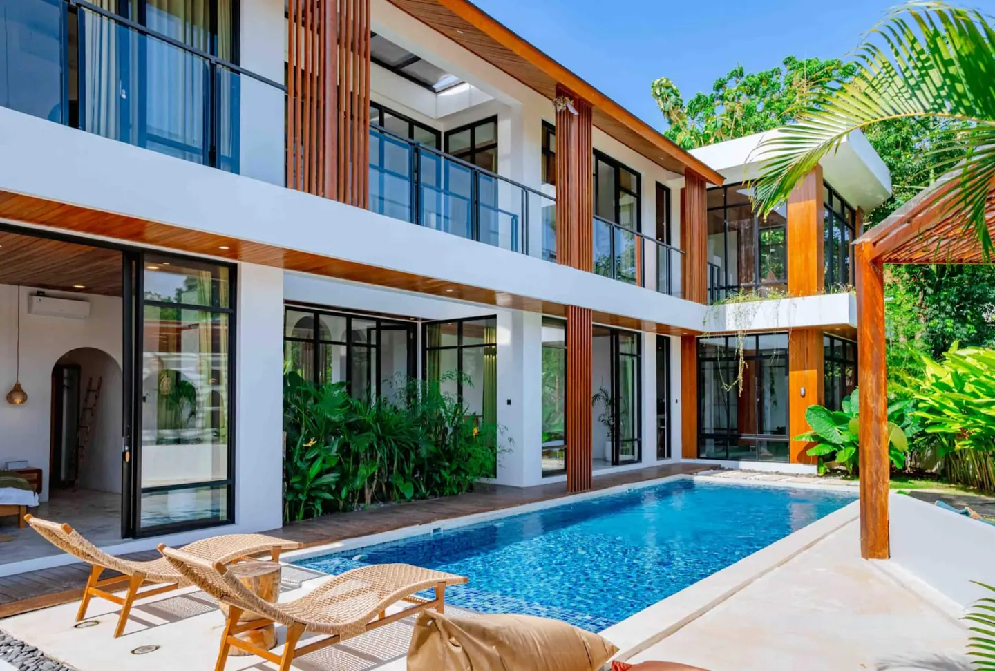 Villa Oliver Uluwatu exterior at golden hour, two-storey villa with teak louvers, black-framed glass, private pool and rattan loungers